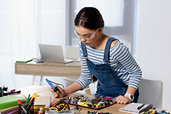 Junge Frau lötet an einem Motherboard und trägt dabei eine Schutzbrille.